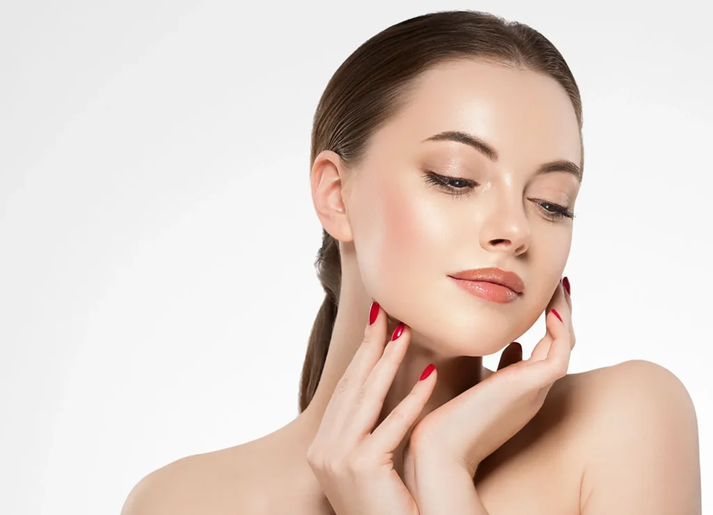 Beautifully healthy woman with dewy skin touching her face and looking off camera.