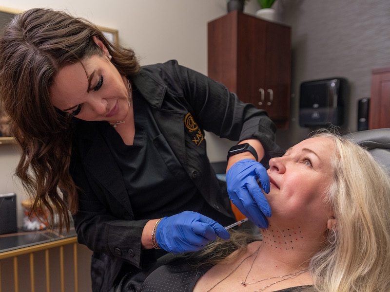 A woman is receiving Kybella injections after looking up "how to get rid of double chin in Fort Collins."
