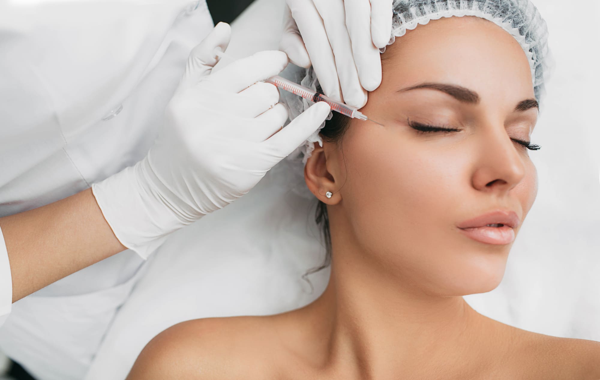 A woman receives a cosmetic injection near her eye from a professional